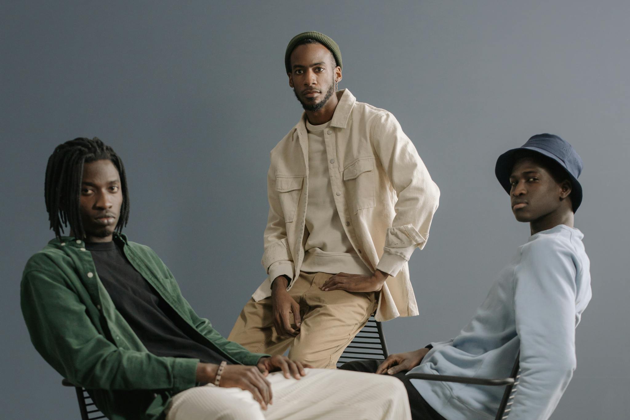 Three stylish men posing in a minimalist studio setting, showcasing modern casual wear.
